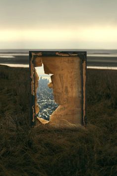 an open door in the middle of a grassy field with a city view behind it