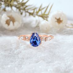 a blue sapphire and diamond ring sitting on top of snow covered ground with flowers in the background