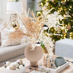 a table topped with a vase filled with white flowers and other decorations next to a christmas tree