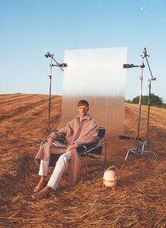 a man sitting in a chair on top of a dry grass field next to two lights