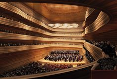 an auditorium filled with lots of people standing on top of a wooden floor next to a stage