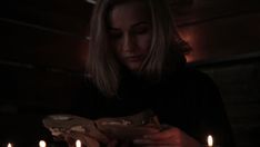 a woman holding a piece of food in front of some candles on a table at night