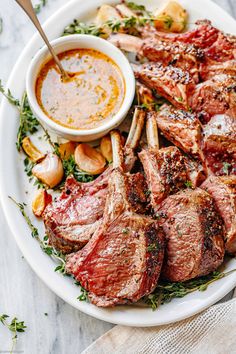 a white plate topped with meat and veggies next to a bowl of dipping sauce