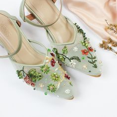 a pair of green shoes with flowers on them next to a pink satin material bag