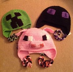 three crocheted hats are laying next to each other on a couch, one is pink and the other is green