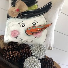 a snowman pillow sitting on top of a wooden bowl filled with pineconis