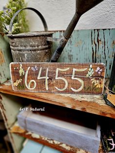 a wooden sign that says 655 with flowers on it and a watering can in the background