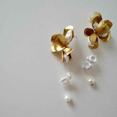 two gold flower earrings with pearls hanging from the ear wires on a white surface,