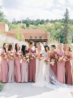 a group of women standing next to each other in front of a building holding bouquets