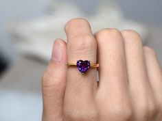 a woman's hand holding a ring with a heart shaped amethyst stone