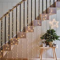 stairs decorated with christmas lights next to a potted plant on a small wooden table