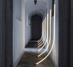 a long hallway with white lights on the walls and concrete flooring in between two buildings