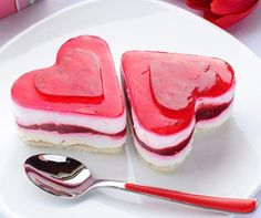 two heart shaped desserts are on a plate with a spoon and red flowers in the background