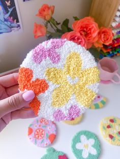 a person holding up a crocheted doily in front of flowers and vases