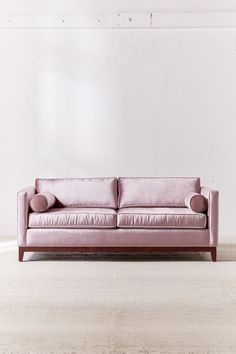 a pink couch sitting on top of a wooden floor next to a white brick wall