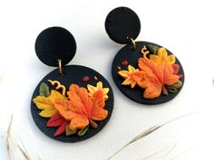 two pairs of black earrings with autumn leaves on them sitting on top of a white surface