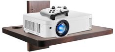 a white projector sitting on top of a wooden shelf next to a video game controller