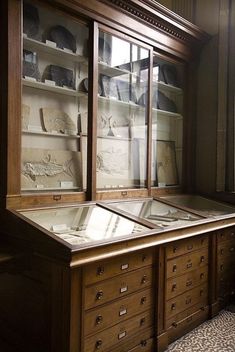 an old wooden cabinet with glass doors and drawers on the front is filled with artifacts