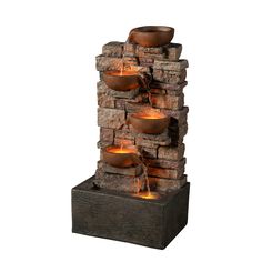 an outdoor water fountain with lit candles on the sides and rocks stacked up to each other