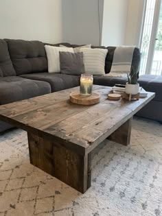 a wooden table sitting on top of a living room floor next to a gray couch