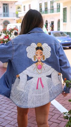 a woman is walking down the street wearing a jean jacket with an image on it