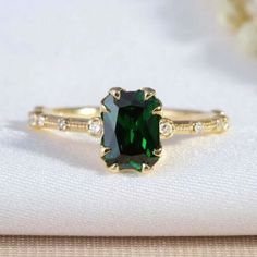 a ring with a green stone surrounded by white diamonds on top of a table cloth