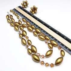 *Description: This is a beautiful mid-century necklace and earring set from the late 1950s. The colors and style are representative of this time period with the large metallic pearled finish oval beads with topaz Austrian Crystals as accent beads. The matching earrings have one crystal in the middle and six of the gold metallic beads around the center in a flower design. The necklace has aurora borealis rhinestone bars near each end. This is a great mid-century set to add to your favorite vintag Vintage Gold Jewelry With Polished Beads, Vintage Gold Jewelry With Large Beads, Vintage Gold Necklaces With Matching Earrings, Vintage Gold Necklace With Matching Earrings, Vintage Polished Beads Jewelry For Wedding, Retro Round Beads Jewelry For Party, Retro Round Bead Jewelry For Parties, Vintage Large Beaded Jewelry For Parties, Retro Beaded Evening Jewelry