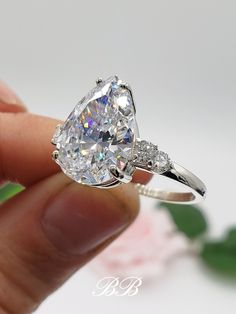 a person holding an engagement ring with a diamond in it's center and side stones on the band