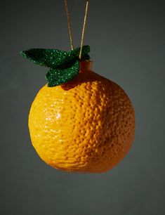 an orange with a green leaf hanging from it's side on a string in front of a gray background