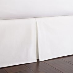 a white bed skirt with two pleated edges on the top and bottom, in front of a wooden floor