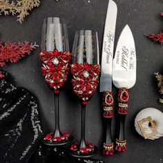 three wine glasses decorated with red and gold beads are sitting next to a knife, fork and spoon rest on a black surface