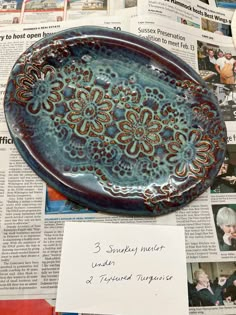 a blue plate sitting on top of a newspaper next to a piece of paper with writing