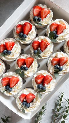 cupcakes with strawberries and blueberries in a white box on a table