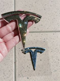 a hand holding a pin with the logo of a tesla car on it's side