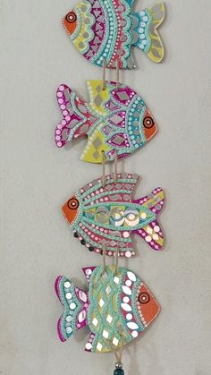 three colorful fish are hanging from a hook on a white wall with a blue beaded cord