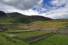 an open field with stone walls and steps leading up to a mountain range in the distance