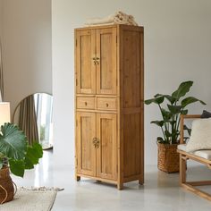 a wooden cabinet sitting in the middle of a living room next to a chair and potted plant