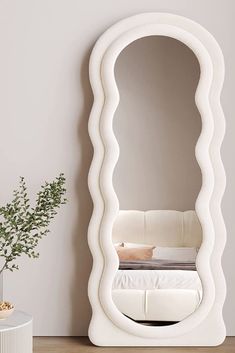 a large white mirror sitting on top of a wooden floor next to a vase filled with flowers