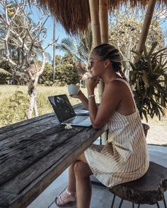 a woman sitting at a picnic table with a laptop on her lap and drinking coffee