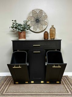 a black cabinet with two bins on top and some plants in the corner next to it