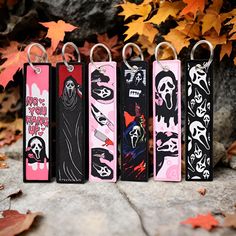 four key chains with different designs on them sitting in front of some leaves and rocks