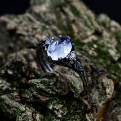 a ring with an oval shaped blue stone surrounded by small white diamonds on top of a mossy rock