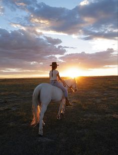 a woman riding on the back of a white horse across a grass covered field at sunset