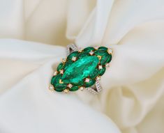 Marquise cut natural emerald and diamond ring in 18k gold. Featuring a vivid green 1.96 carat Colombian emerald center stone. Flanked by a gorgeous cluster of marquise Colombian emeralds and round diamonds. Each Emerald is mounted with sharp 18k Yellow Gold that perfectly contrasts and exaggerates the life and green color hue of the Emerald. This lively deep green color saturation is found only in Emeralds of Colombian origin.  This is a noticeably valuable ring that elongates and hugs the finger. Showcasing unmistakably natural gems that subtly convey the sense of luxury and affluence to those who admire it. Ring Details:  ✔ Metal: 18K Solid Gold (White/Yellow) ✔ Ring Size: 6.5 (adjustable) ✔ Ring Weight: 6.42 Grams ✔ Shank: Split ✔ Total Gemstone Weight: 3.89 CTTW ✔ Setting: Open back, p Luxury Green Marquise Diamond Ring, Green Marquise Diamond Ring Fine Jewelry, Green Marquise Emerald Diamond Ring, Marquise Emerald Diamond Ring In Green, Marquise Cut Rings, Yellow Rings, Colombian Emeralds, Marquise Cut, Natural Emerald