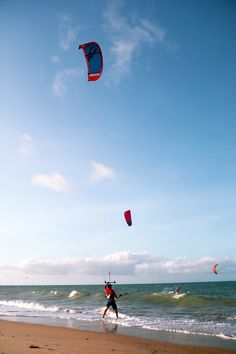 two people on the beach flying kites in the sky over the water and waves