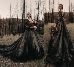 a woman standing in a field wearing a long black dress with flowers on the skirt