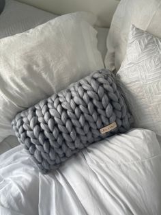 a gray knitted pillow sitting on top of a white bed