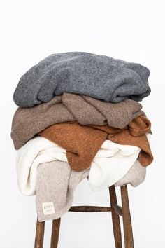 several blankets stacked on top of each other in a wooden stool against a white background