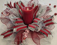 a red candle sitting on top of a mesh wreath with ribbons and beads around it