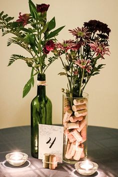 two vases with flowers in them sitting on a table next to candles and wine bottles